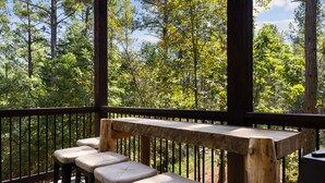 A wooden deck with a bench and stools, overlooking a forested area. - Broken Bow Luxury Cabin Hot Tub Playset Games (Broken Bow)