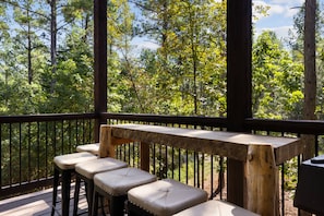 A wooden deck with a bench and stools, overlooking a forested area.