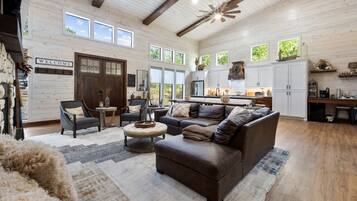 A spacious living room with a large brown leather sofa, a fireplace, and a dining area with a kitchen in the background.