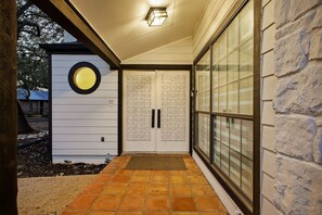 Ein überdachter Eingangsbereich mit Fliesenboden, einem Rundfenster und einer Tür mit Musterdesign.
