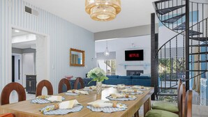 A dining area with a long table, chairs, a vase with flowers, and a television displaying 'NETFLIX' in the background. - Riverwalk Villa Game Room Grill Heated Pool (San Antonio)