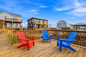 Una terraza de madera con tres sillas Adirondack, vista a casas y cielo despejado.
