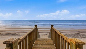 Ein hölzerner Steg führt zu einem Strand unter blauem Himmel.