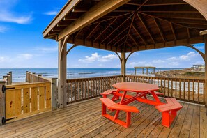 A wooden deck with a picnic table and benches overlooking the ocean. - Steps to the Sand Sleeps 12 Hot Tub Grill (Sneads Ferry)