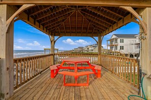 A wooden deck with a covered seating area overlooking the beach. - Steps to the Sand Sleeps 12 Hot Tub Grill (Sneads Ferry)