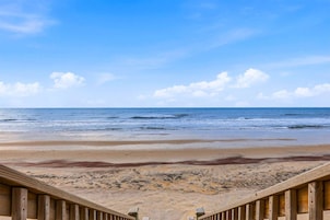 Una terraza de madera que da a una playa de arena, con el océano al fondo.