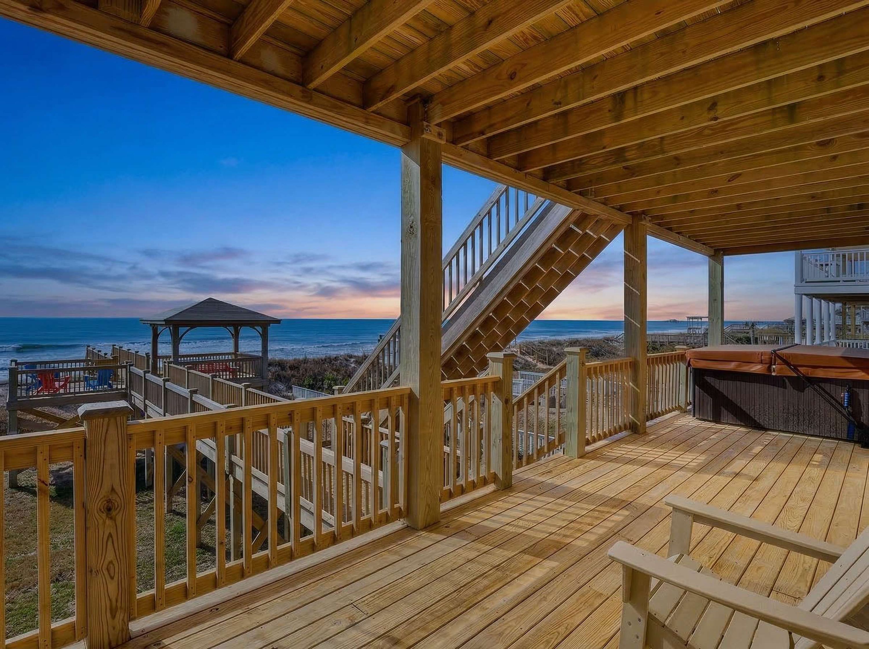 A wooden deck with a view of the ocean, a gazebo, and a covered seating area.