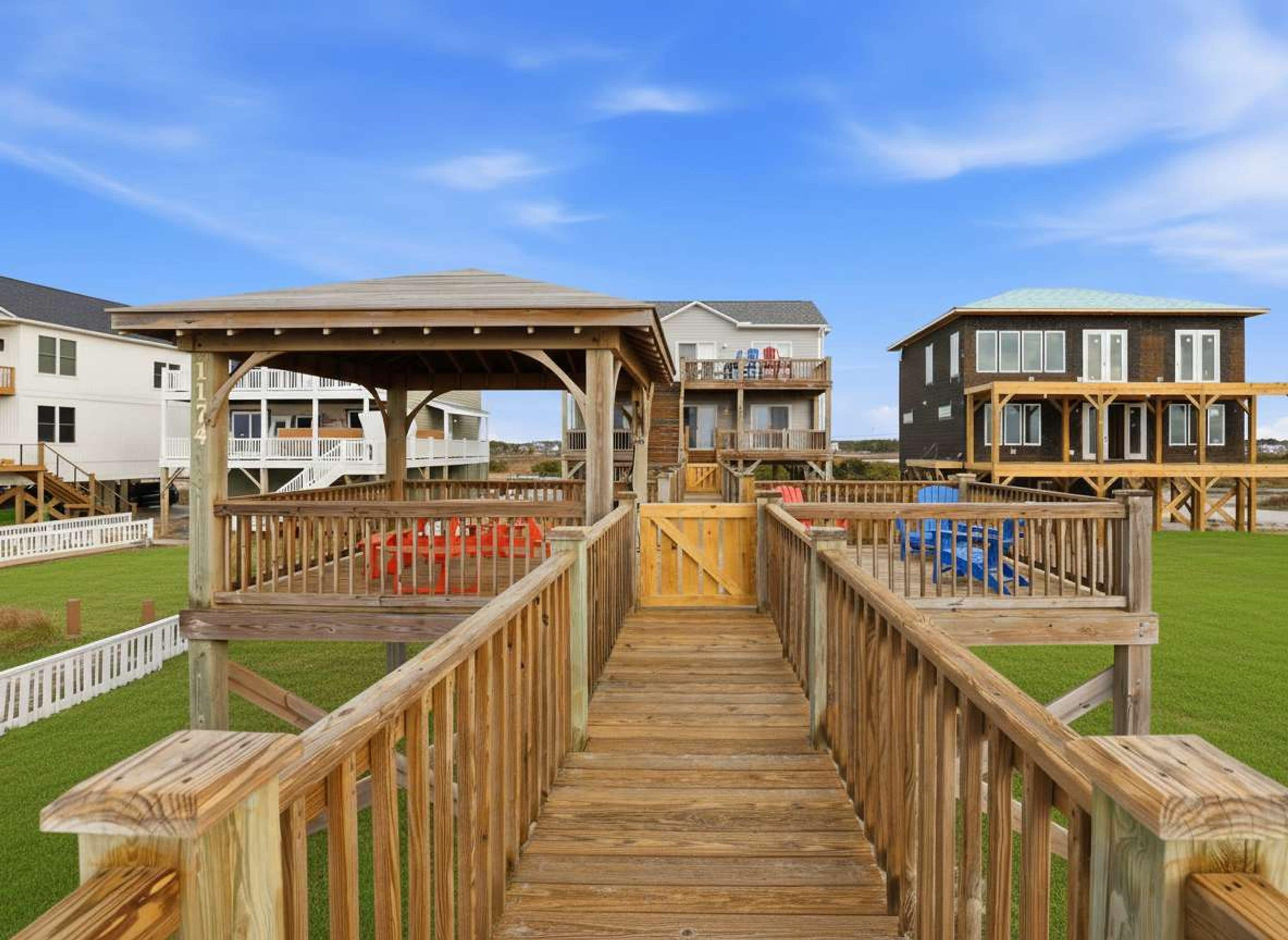 A wooden deck leading to a building with a covered area and a second building in the background.