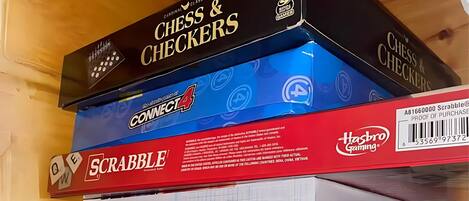 A stack of board games including Chess & Checkers, Connect4, Scrabble, and Battleship.