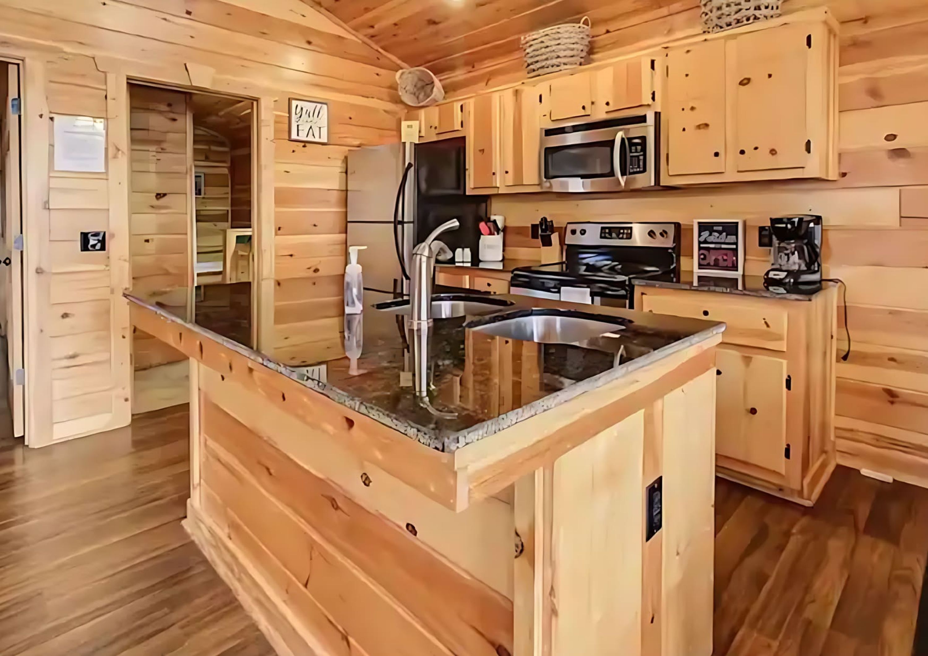 A wooden cabin interior with a kitchen featuring a central island, stainless steel appliances, and a sign on the wall.