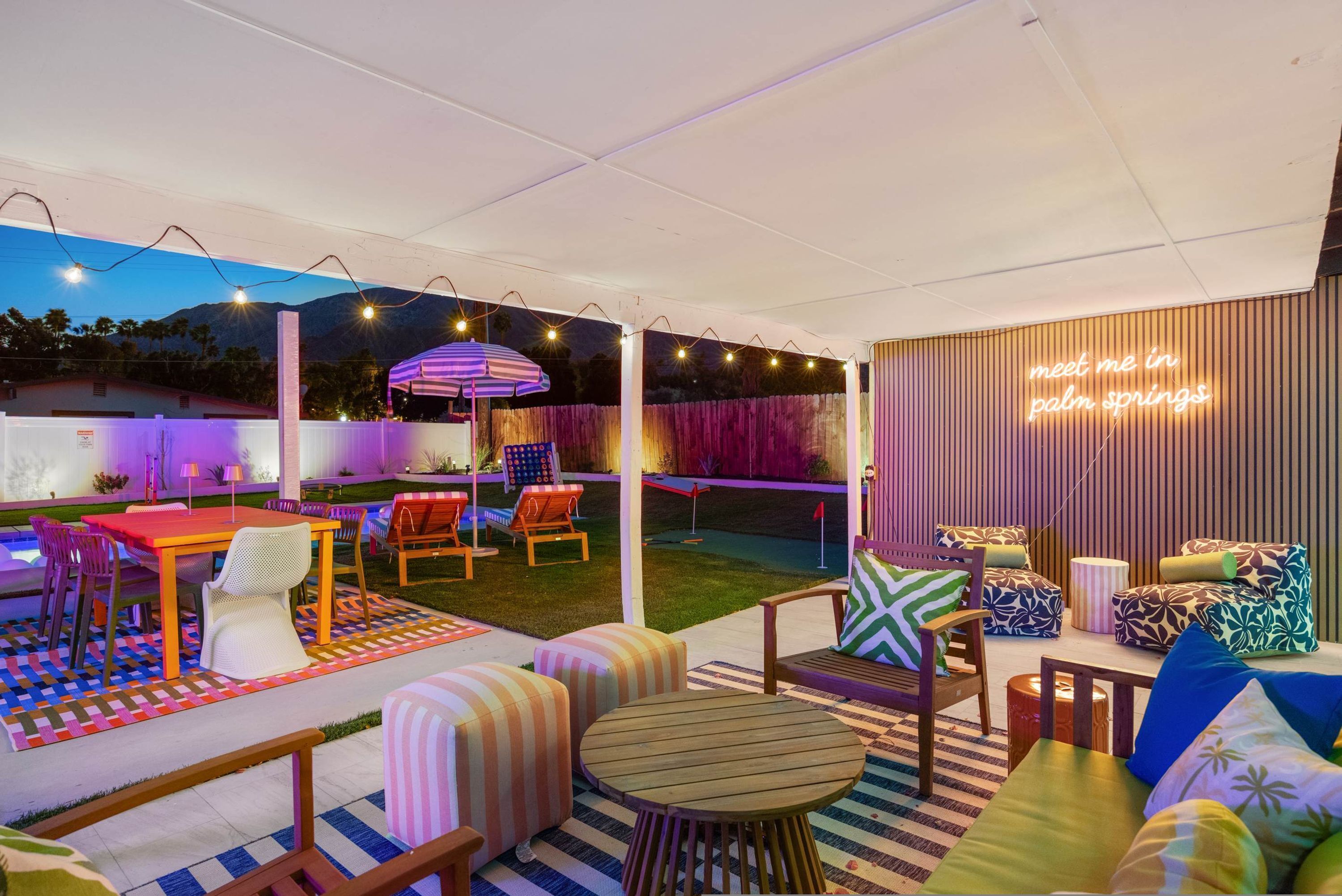 Un espace extérieur aménagé en terrasse, avec une table et des chaises, un parasol à rayures et un panneau lumineux au néon.