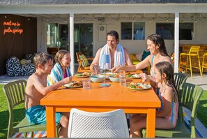 A family dining outdoors at a table with a view of a building with a sign that reads 'meet me in palm springs'. - Peaks Palms Oasis - Heated Pool - Games (Palm Springs)