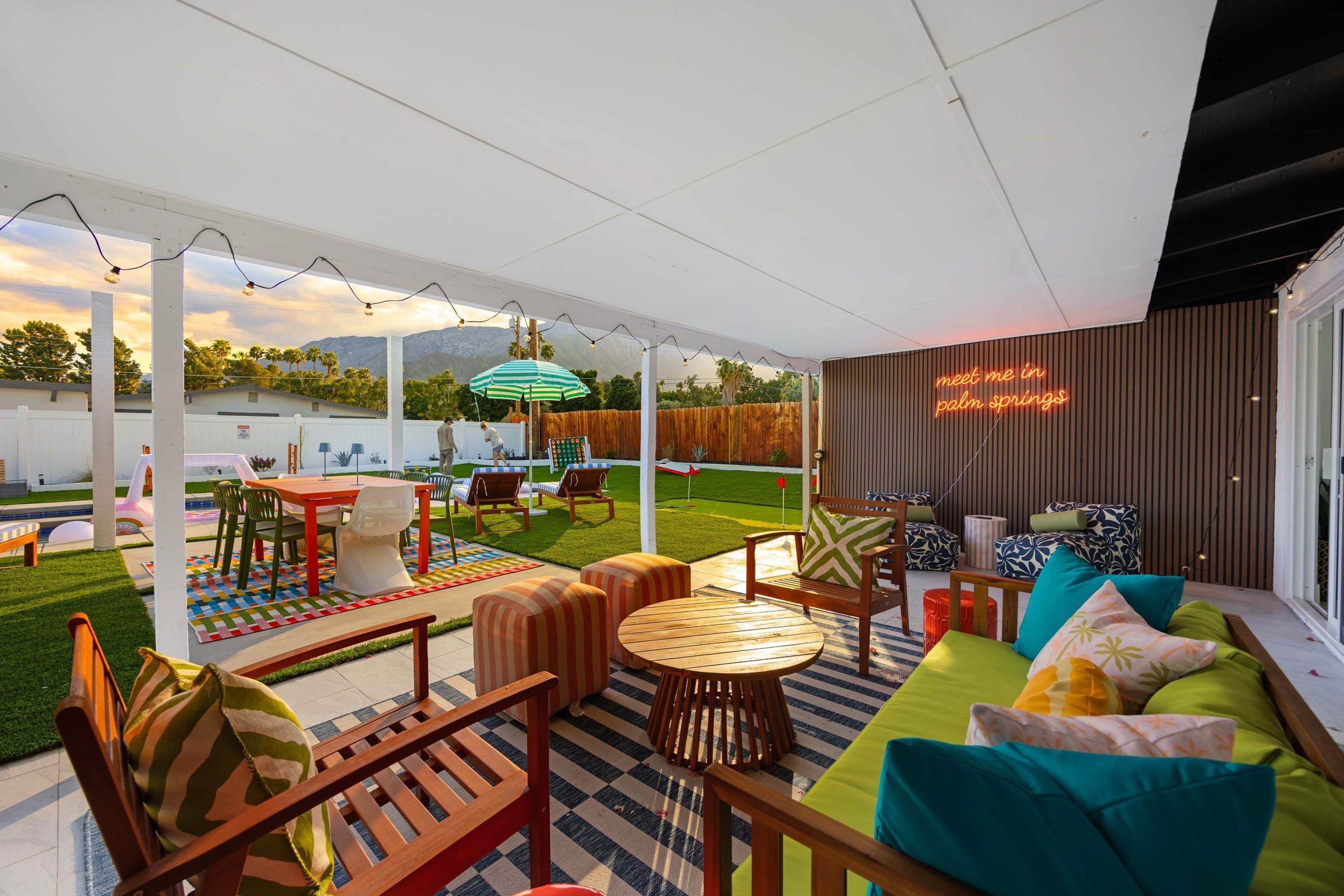 Un espacio al aire libre con patio, piscina, sillas de descanso y un letrero de neón.