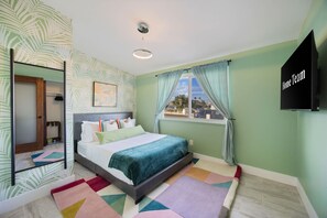 Ein Schlafzimmer mit einem Bett, einem Fenster mit Vorhängen, einem Wand-Fernseher und einer Wandgestaltung mit Muster.