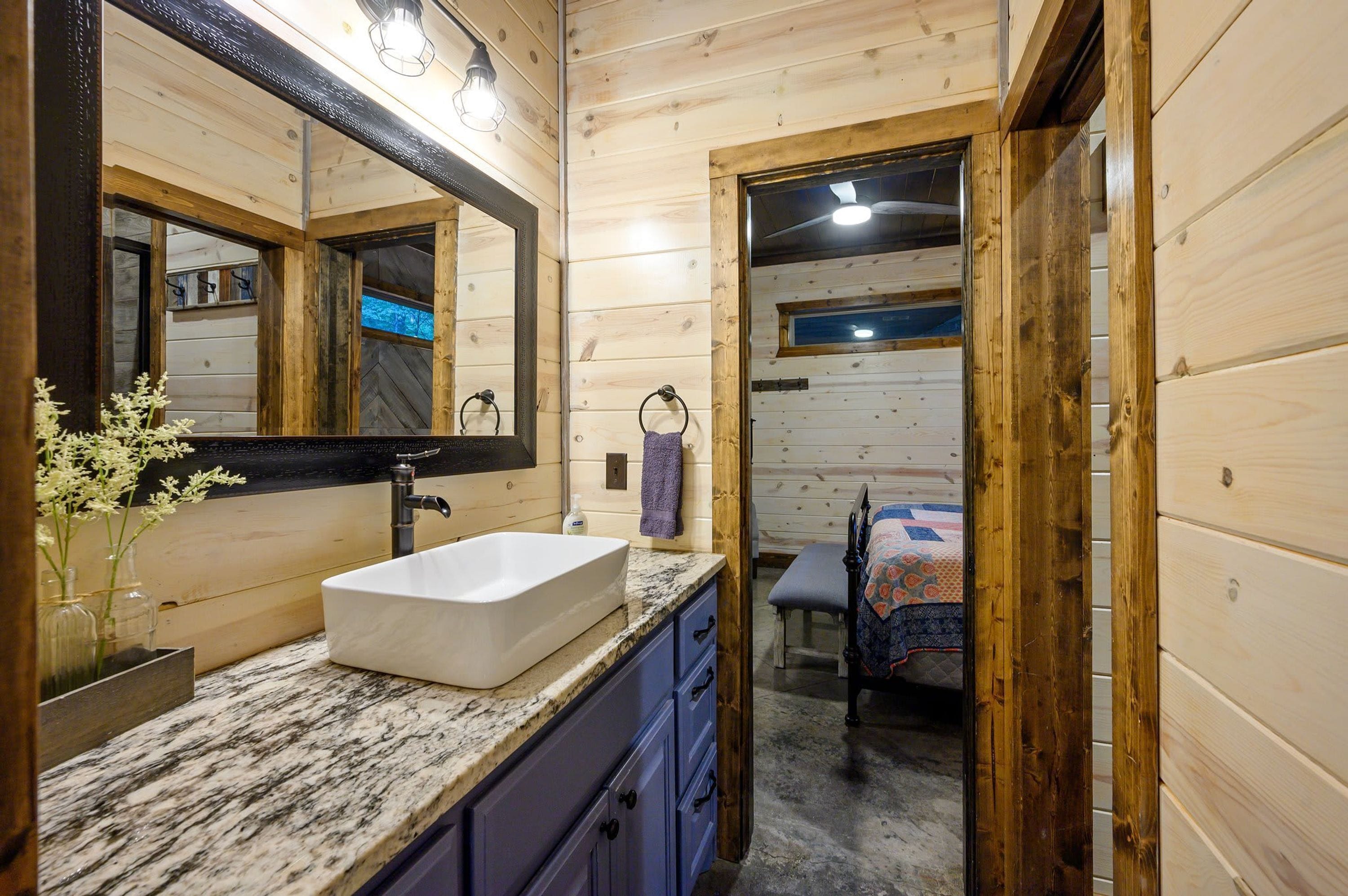 Interior de una cabaña de madera con encimera de mármol, un lavamanos blanco y un espejo grande.