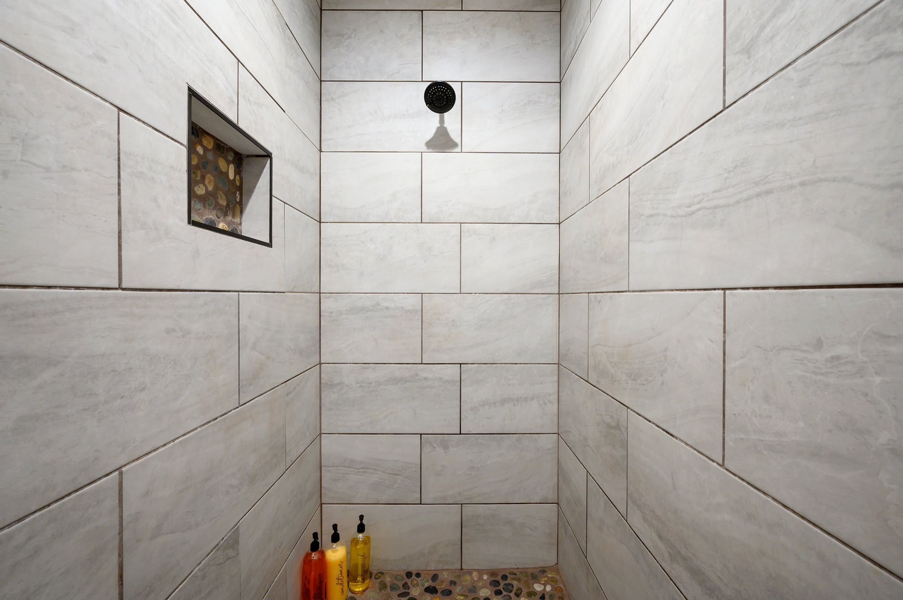 A shower with white tiles, a showerhead, and three bottles of liquid at the bottom.
