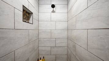 A shower with white tiles, a showerhead, and three bottles of liquid at the bottom.