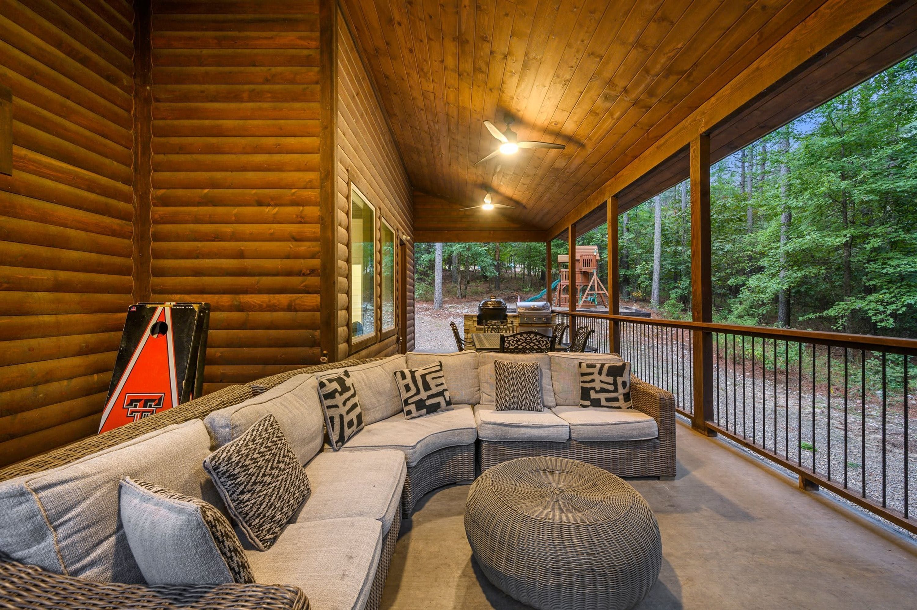 A log cabin with a covered porch, a sectional sofa, and a view of the forest.