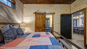 A bedroom with a large bed, a wooden door, and a view of a kitchen area.