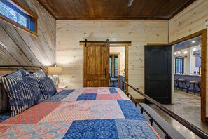 A bedroom with a large bed, a wooden door, and a view of a kitchen area. - Aspen Creek Lodge Spacious Luxury Cabin Retreat (Broken Bow)
