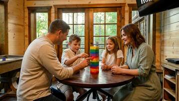 A family playing with a colorful block tower in a wooden room with large windows.