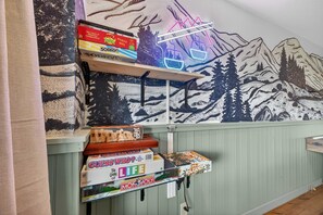 A wall with a mountain-themed mural and shelves holding board games. - Mins to Hatley Pointe Hot Tub Views Sauna (Mars Hill)