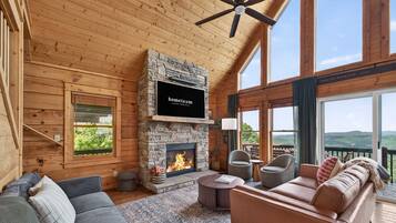 A cozy interior with a stone fireplace, a sofa, a chair, and a view of the outdoors.