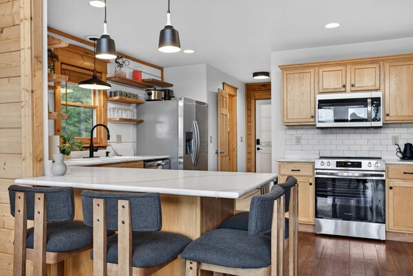 A modern kitchen with a central island, wooden cabinets, stainless steel appliances, and a seating area with chairs. - Mins to Hatley Pointe Hot Tub Views Sauna (Mars Hill)