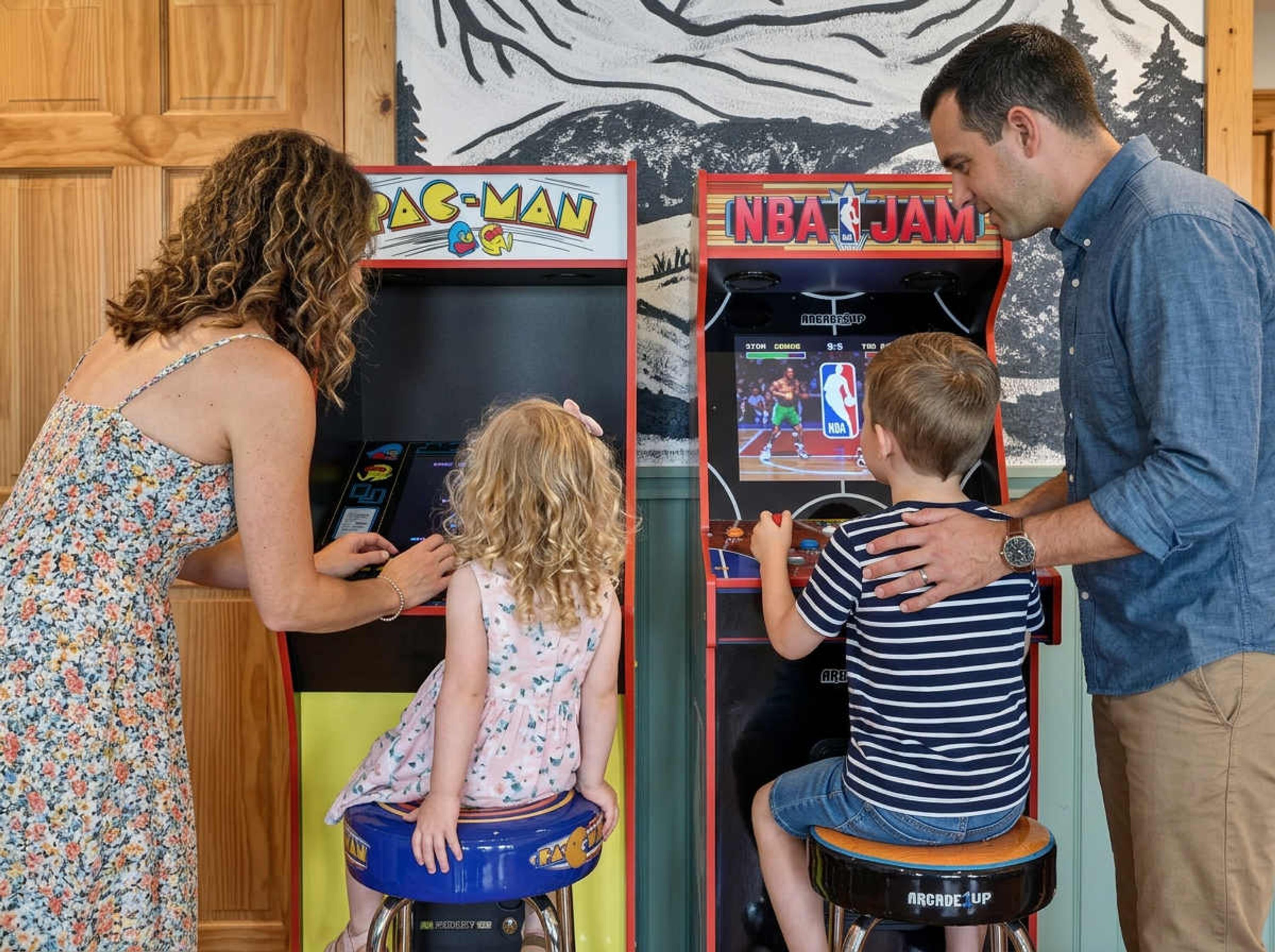 Uma família se divertindo em jogos de fliperama, incluindo Pac-Man e NBA Jam.