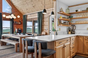 A wooden cabin interior with a dining area, kitchen, and a view of the outdoors. - Mins to Hatley Pointe Hot Tub Views Sauna (Mars Hill)
