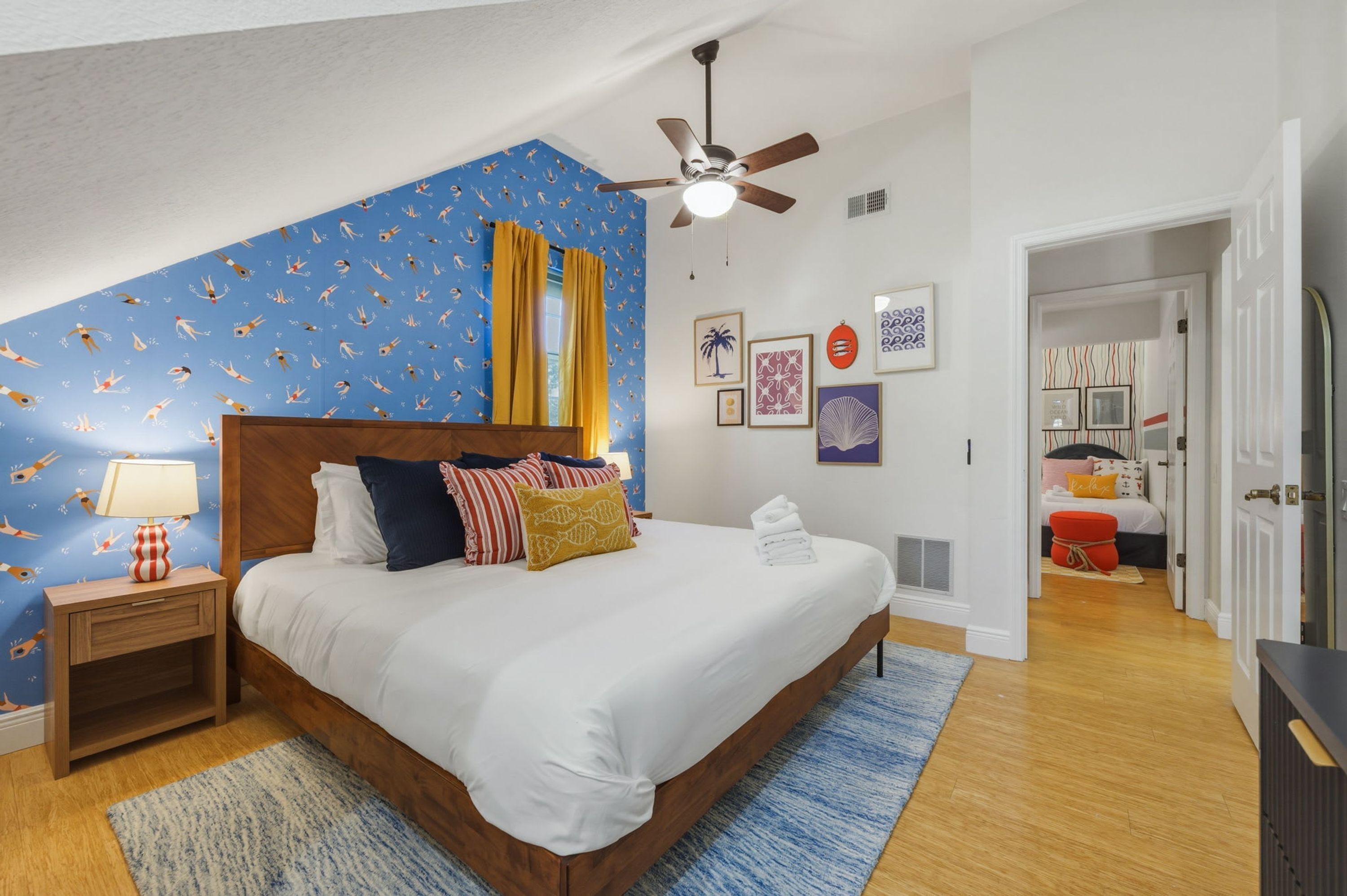 A bedroom with a bed, a nightstand, a lamp, a ceiling fan, and a window with curtains.