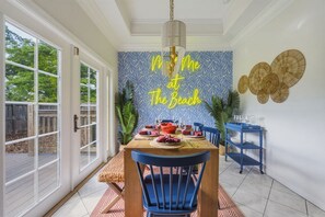 A dining area with a table set for four, a blue chair, and a wall with a tropical leaf pattern and a neon sign. - Sleeps 10 Heated Pool Game Room Hot Tub (Largo)
