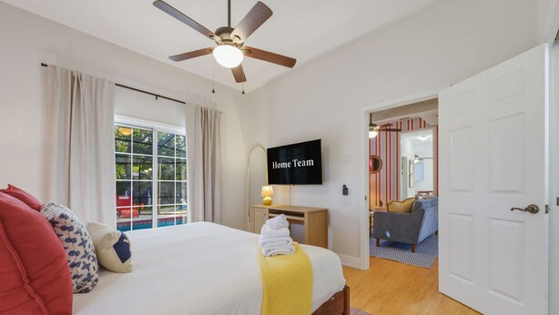 Ein Schlafzimmer mit Bett, Deckenventilator, Fernseher und Blick ins Freie.