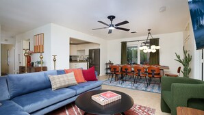 A modern living room with a blue sofa, a green armchair, a coffee table, and a dining area with a table and chairs. - Starcrest 4 Br Haven Pool Hot Tub Putt Putt Arcade (San Antonio)