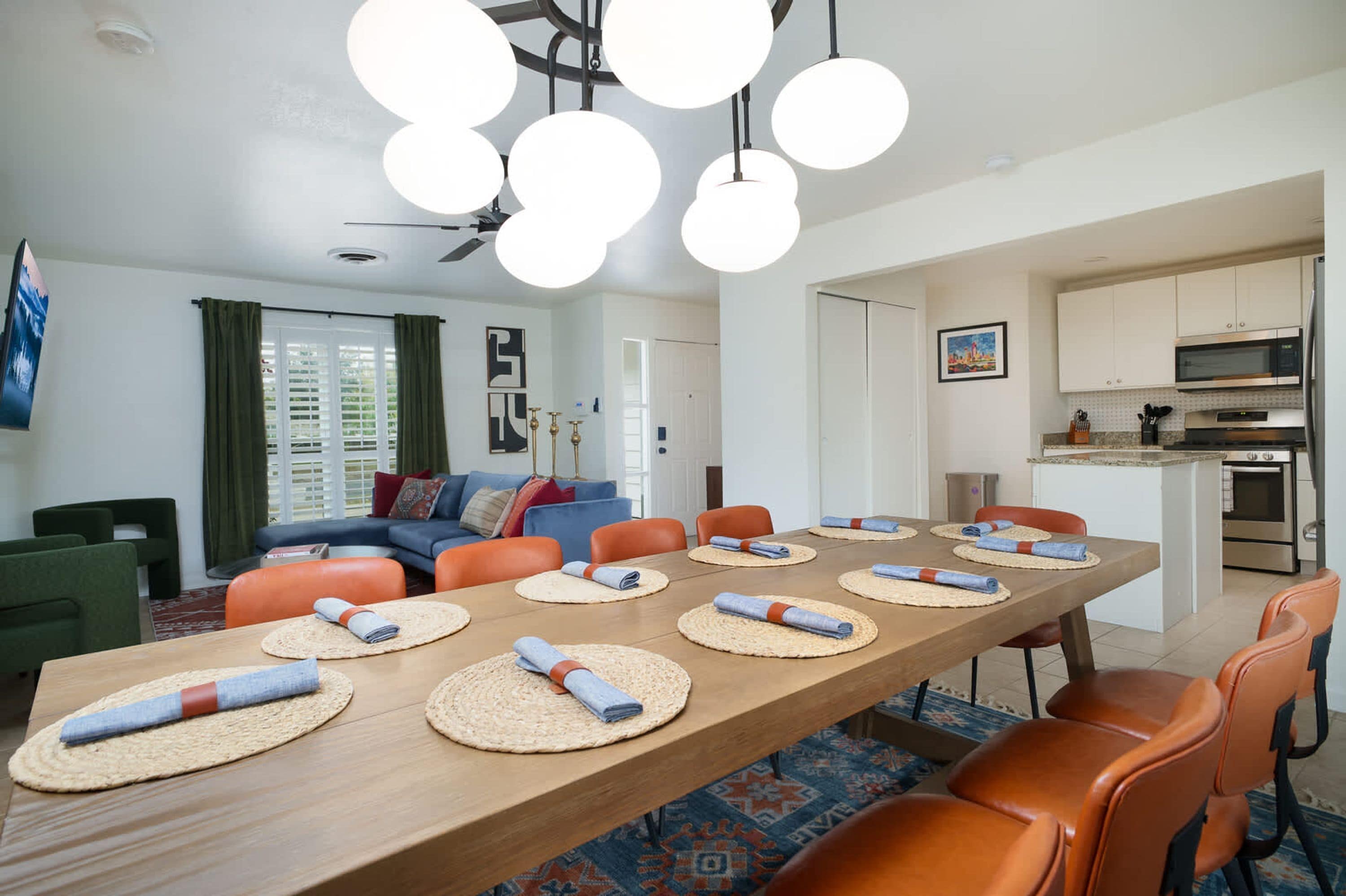 A modern living room with a wooden dining table, orange chairs, and a blue sofa.