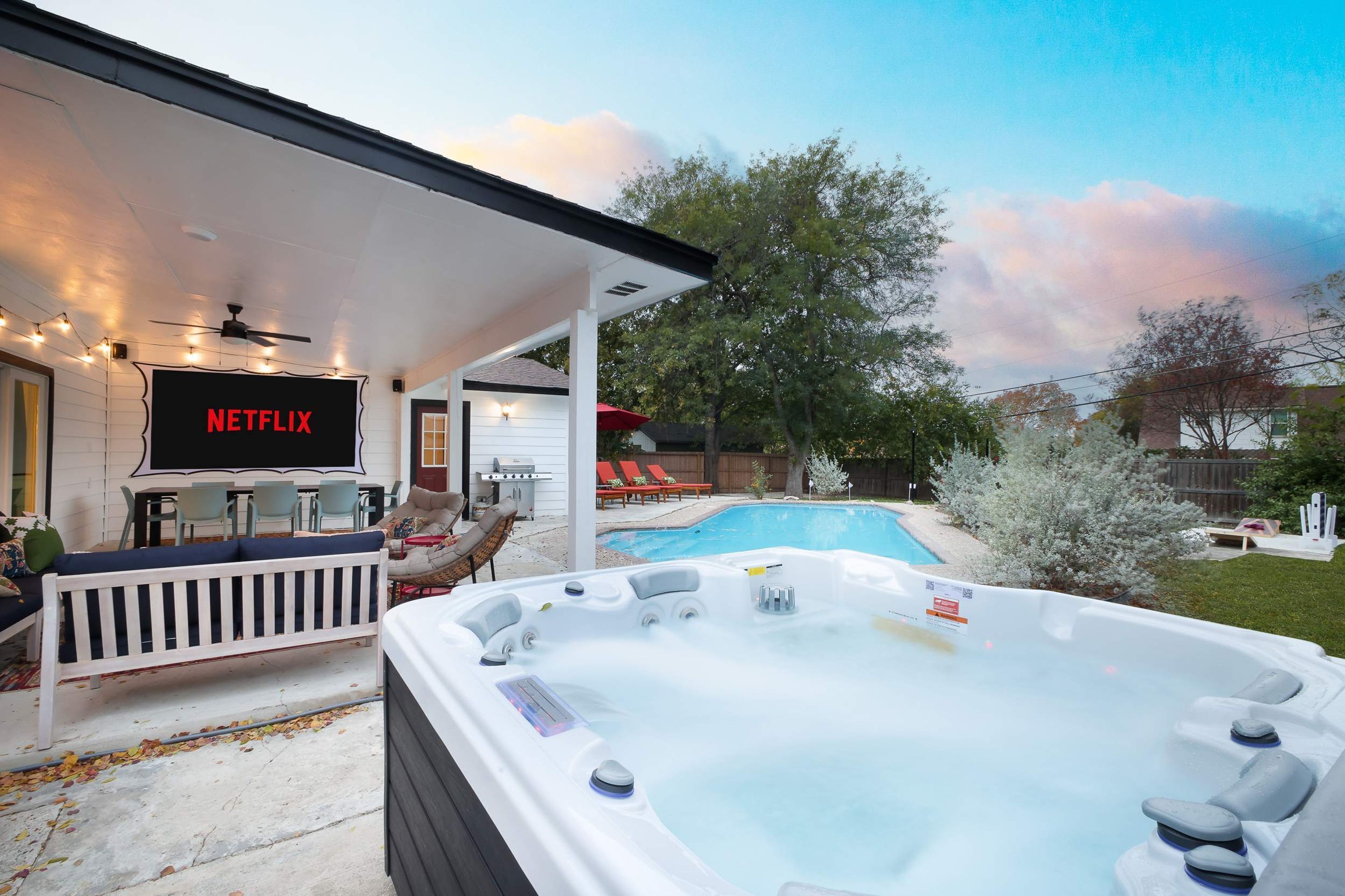 A backyard with a hot tub, a pool, outdoor furniture, and a TV screen displaying 'NETFLIX'.