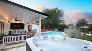 A backyard with a hot tub, a pool, outdoor furniture, and a TV screen displaying 'NETFLIX'. - Starcrest 4 Br Haven Pool Hot Tub Putt Putt Arcade (San Antonio)
