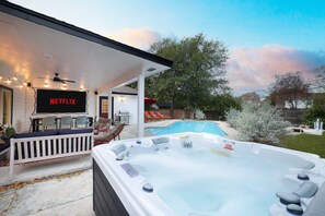 Ein Garten mit Whirlpool, Schwimmbad, Gartenmöbeln und einem Fernseher, der 'NETFLIX' anzeigt.