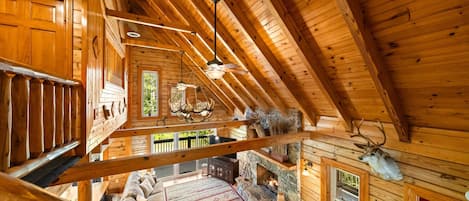 Interior de una cabaña de madera con habitación en altillo, chimenea de piedra y cornamentas de venado en las paredes.