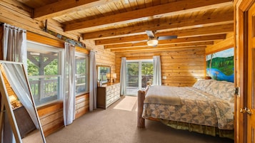 Quarto de cabana de madeira com cama, escrivaninha e janela com cortinas.