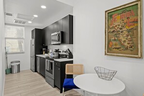 Een compacte keuken met moderne apparaten, een eethoek met een simpele tafel en stoel, en een vintage kaart aan de muur.