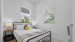 Una camera da letto con un letto, due comodini con lampade, un termosifone e finestre con tende.