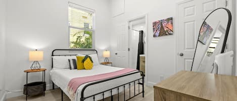 A bedroom with a bed, bedside lamps, a window with blinds, a door, and a mirror.