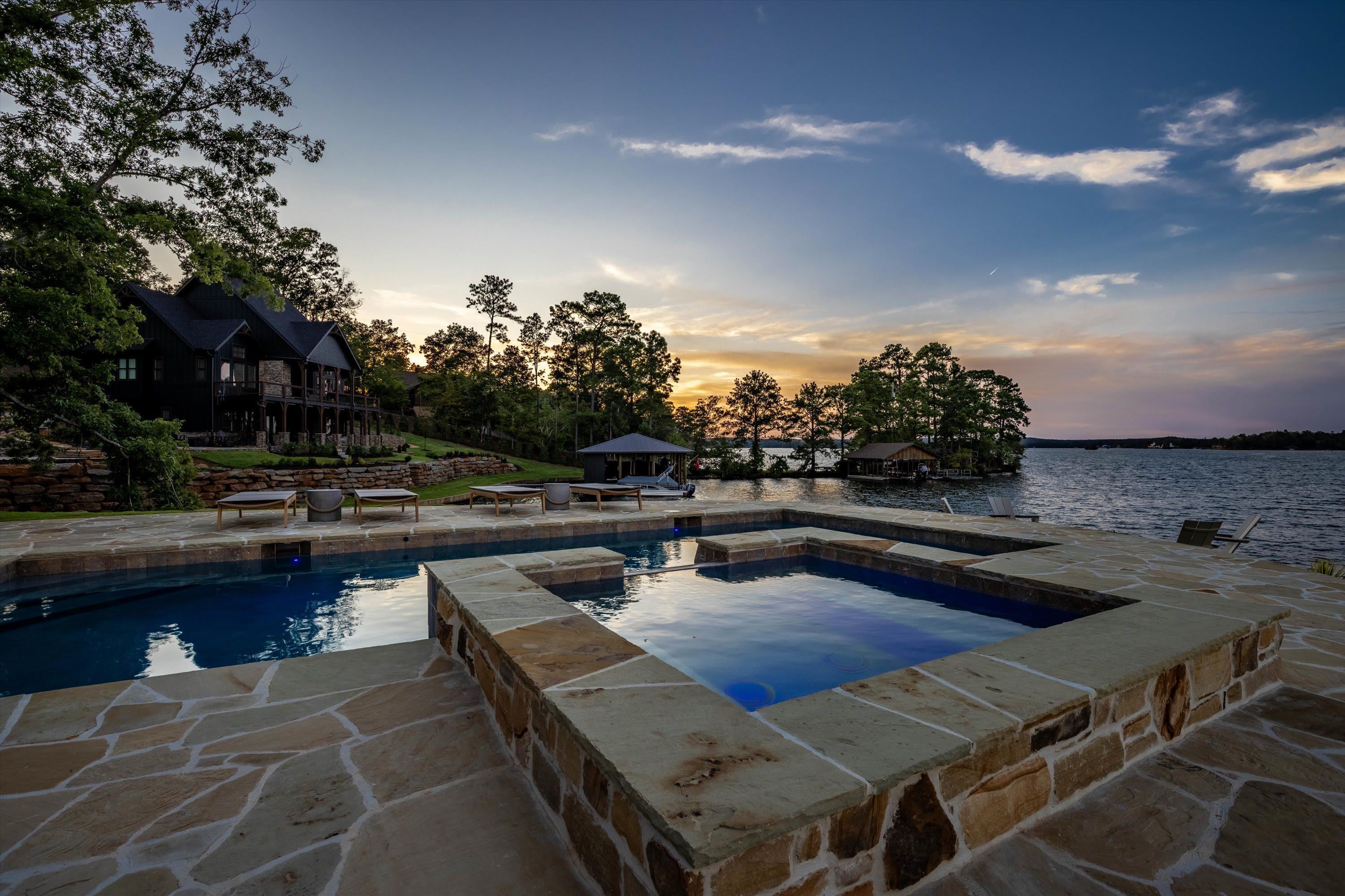 A swimming pool with stone borders, a wooden deck, and lounge chairs.