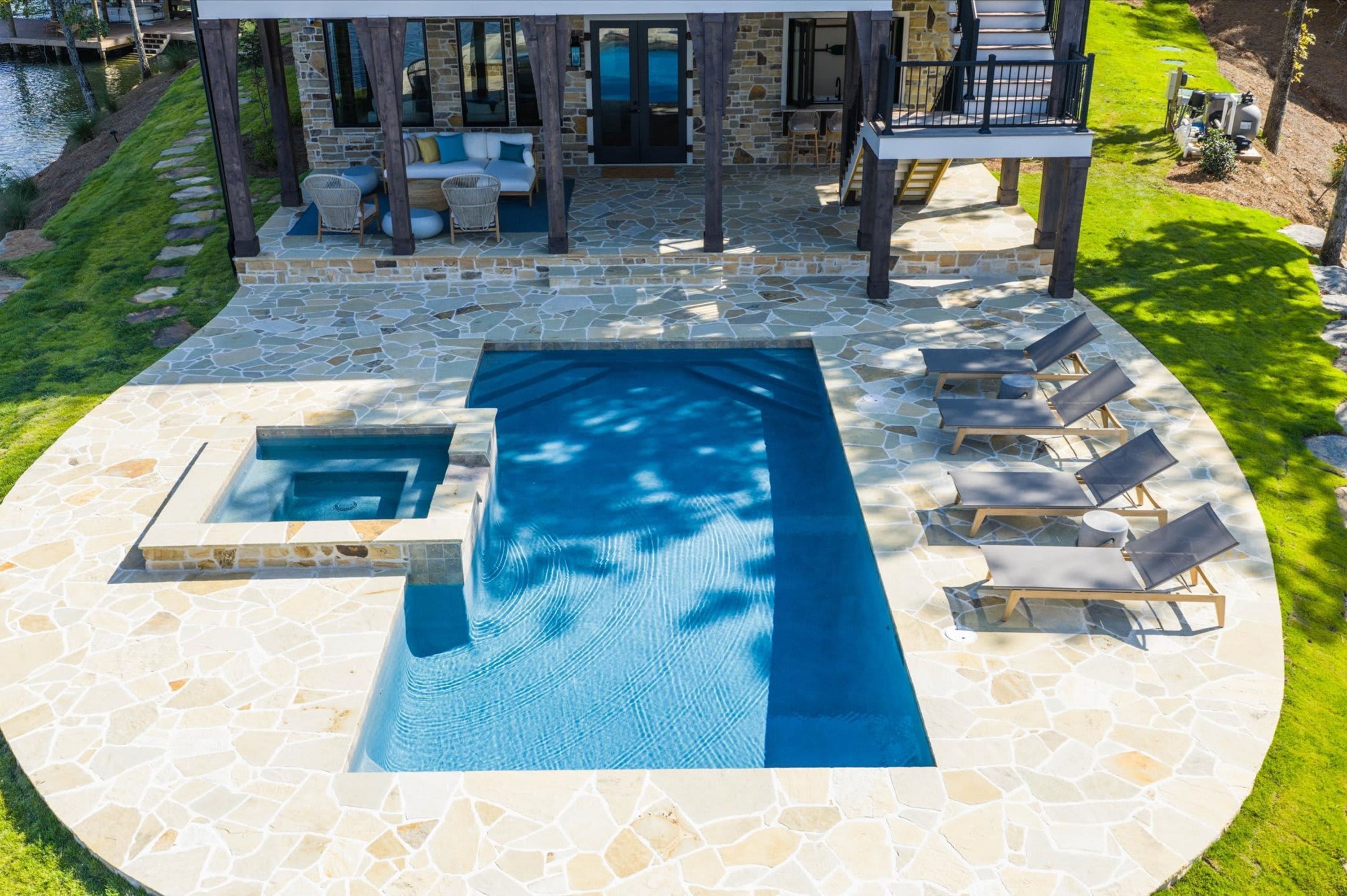 A swimming pool with a stone deck, lounge chairs, and a covered seating area.
