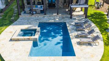 A swimming pool with a stone deck, lounge chairs, and a covered seating area.