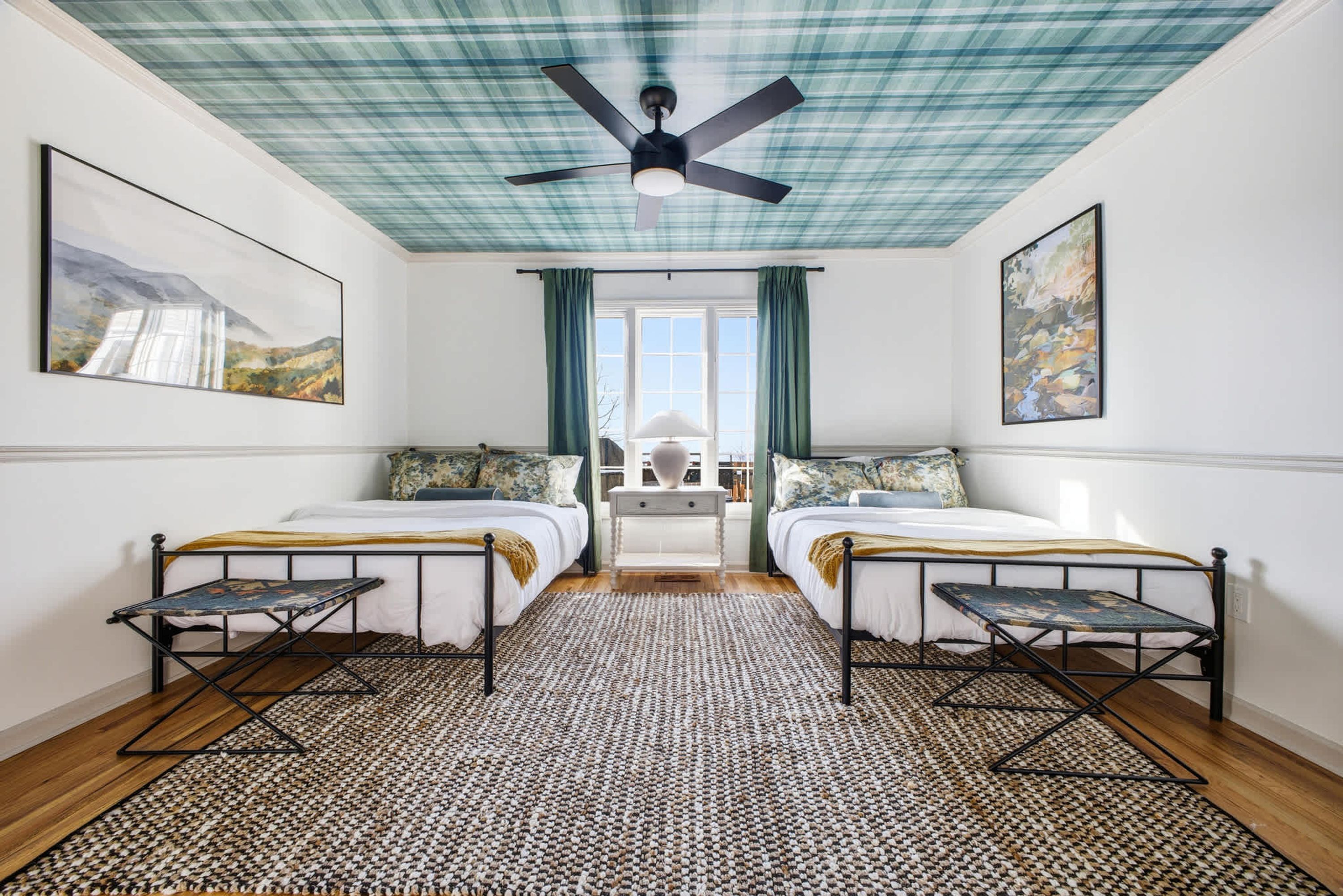 A room with two beds, a ceiling fan, and artwork on the walls.