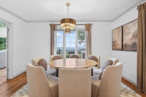A dining area with a round table, six chairs, a chandelier, and a view through large windows. - Luxury Mtn Retreat Hot Tub Sleeps 18 Game Room (Asheville)