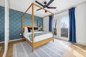 A four-poster bed with a wooden frame and a ceiling fan, a large window with blue curtains, and a patterned wallpaper. - Luxury Mtn Retreat Hot Tub Sleeps 18 Game Room (Asheville)