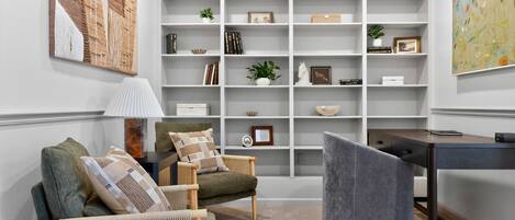 A modern living room with a bookshelf, a desk, and a comfortable seating area.